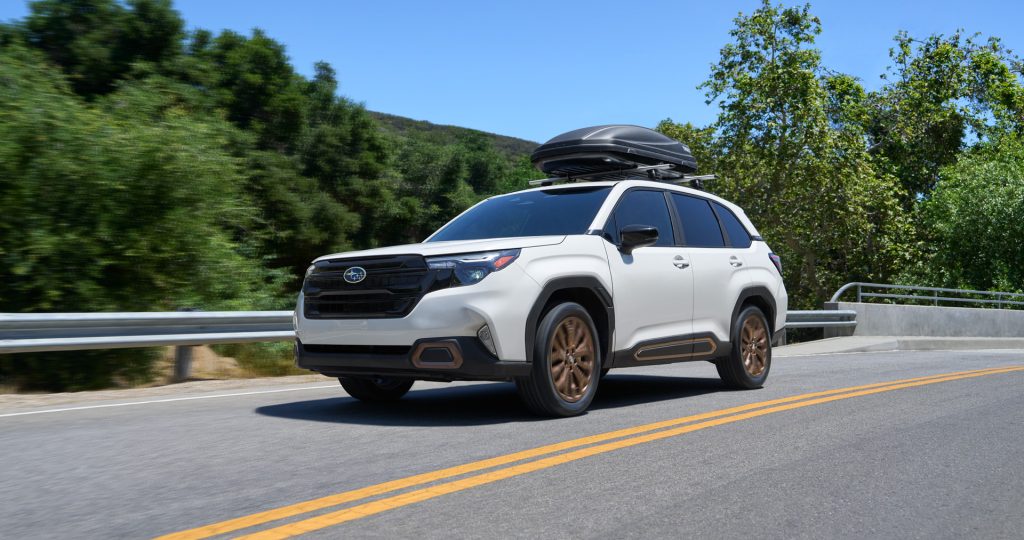 2026 Subaru Forester compact SUV on the road with roof cargo box, showcasing standard all-wheel drive, spacious utility, advanced safety features, and adventure-ready performance.