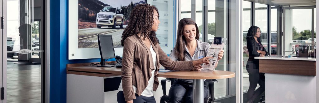 Customer reviewing lease offers with a dealership representative inside a modern auto showroom.
